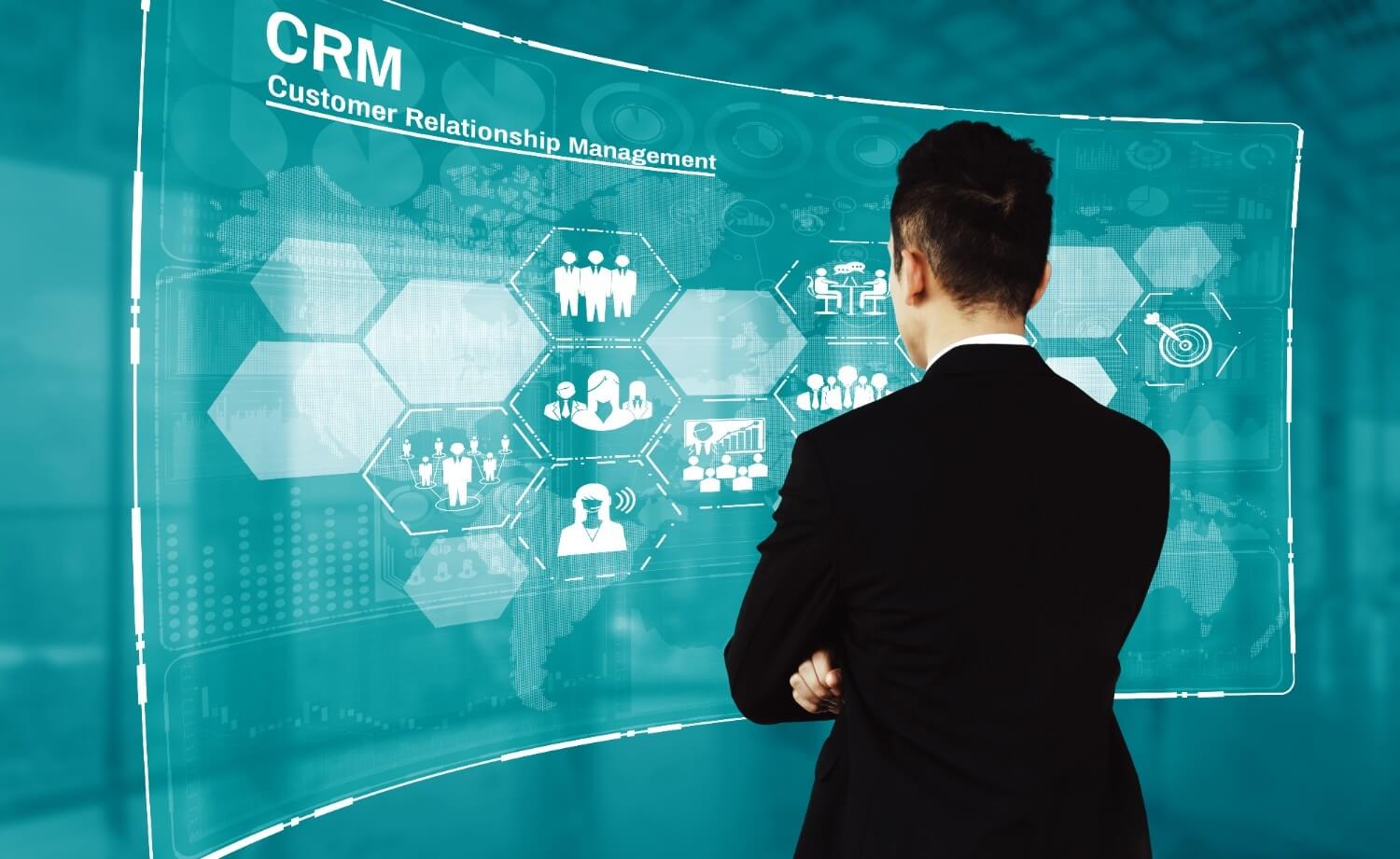 Business professional standing in front of a large digital CRM dashboard displaying customer relationship management icons, data charts, and analytics.