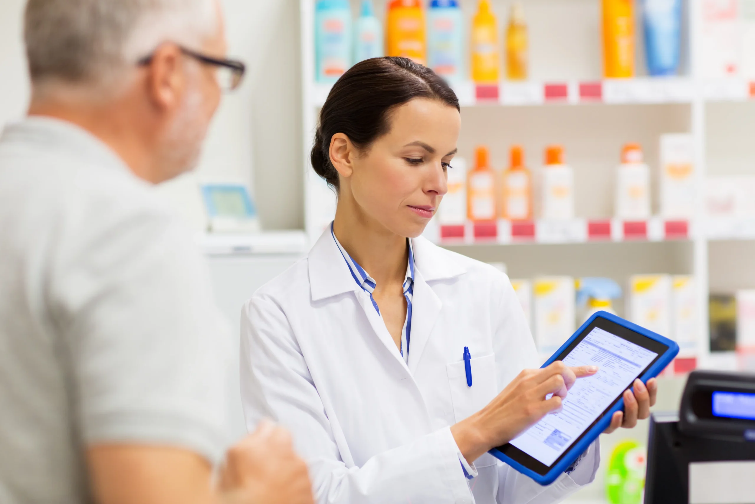 Pharmacist assisting an elderly patient using a tablet equipped with Pharmacy Workflow Automation.