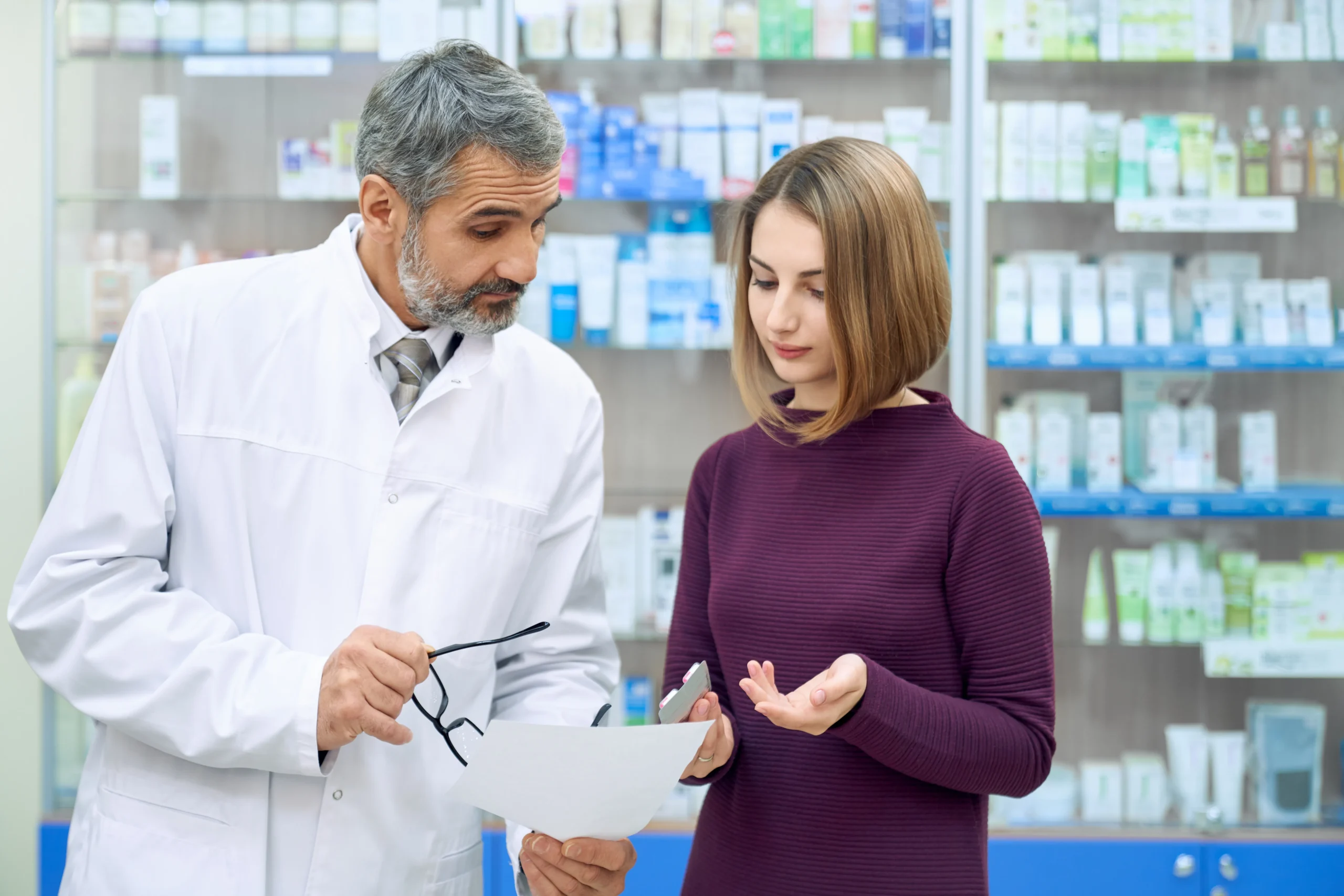 Senior pharmacist reviewing patient care plan notes with a customer using specialty pharmacy CRM.