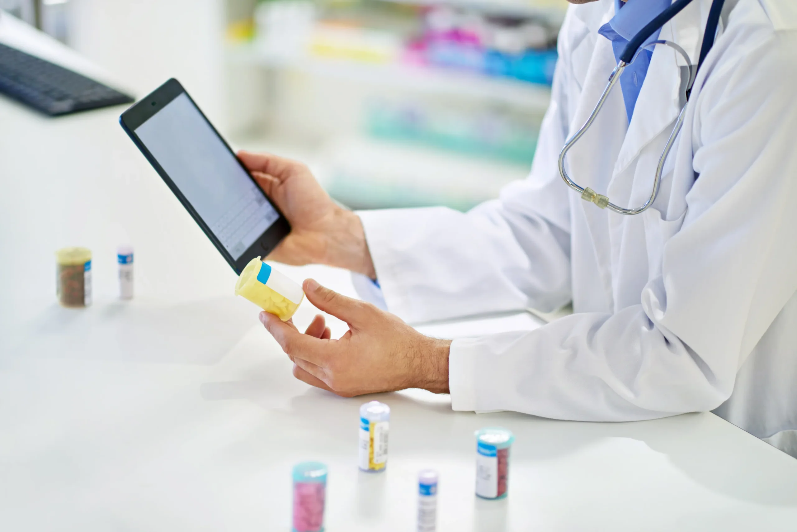 Pharmacist holding a medicine bottle while managing outreach preferences on a digital tablet via pharmacy patient engagement software.